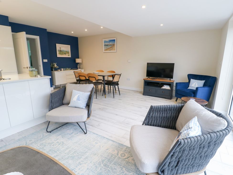 A living room with a sofa, armchair, dining table and television at 2 Lon Y Dryw in Trearddur Bay