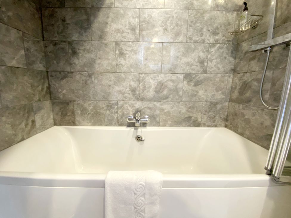 A bathtub with a showerhead and towel in a bathroom at Meadfoot Bay Apartment at Hesketh Crescent, Torquay