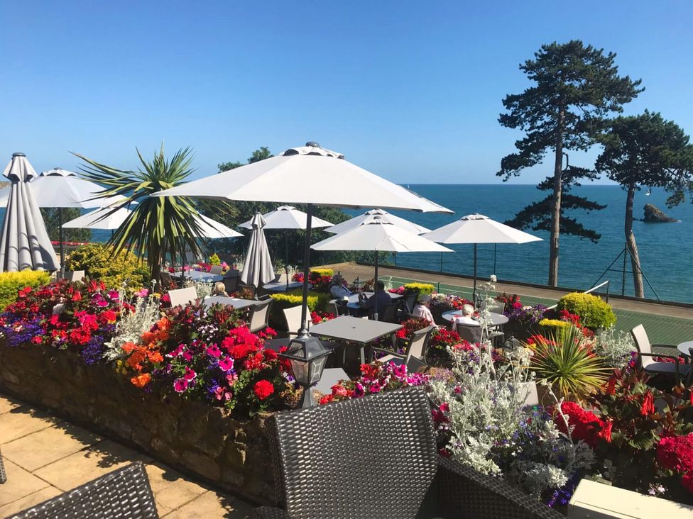 An outdoor seating area with umbrellas and flowers at Meadfoot Bay Apartment at Hesketh Crescent in Torquay