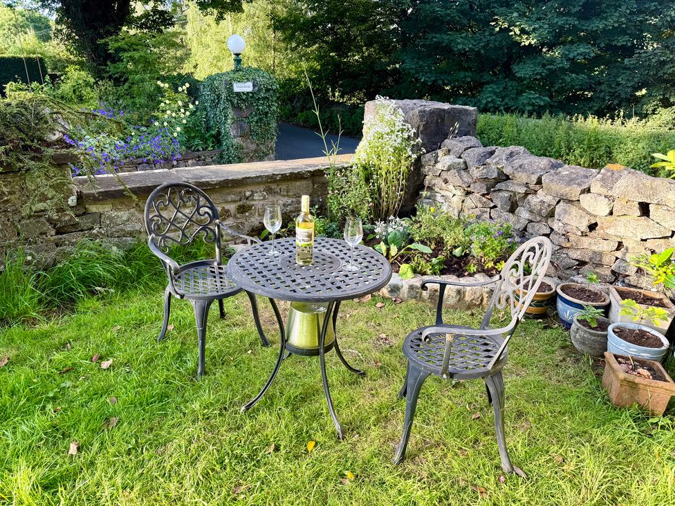 A garden with a table, chairs, wine, and flower pots at The Treetop in Giggleswick near Settle