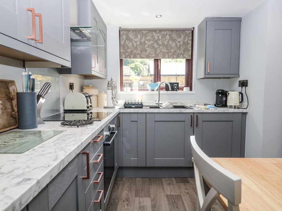 A kitchen with gray cabinets and appliances at Dolly Blue Backbarrow near Newby Bridge