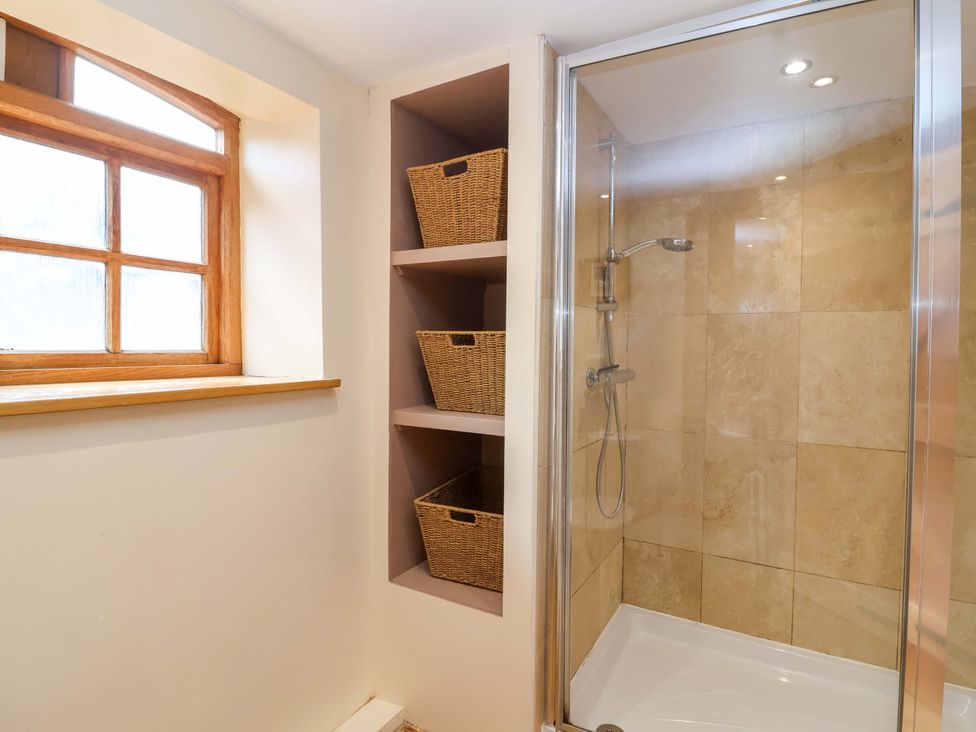 A bathroom with a shower and storage shelves at Millbarn in Crowcombe