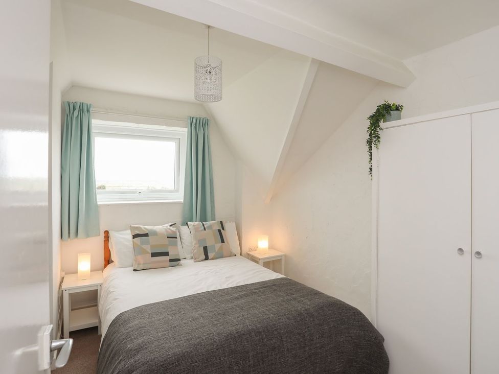 A bedroom with a bed, curtains, and a wardrobe at Penrhyn - 4 Ty'n Don