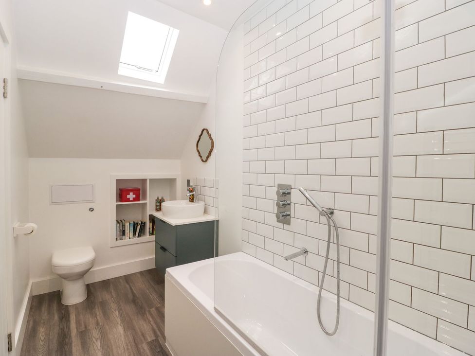 A bathroom with a bathtub, toilet, sink and shelves at The End in Langport