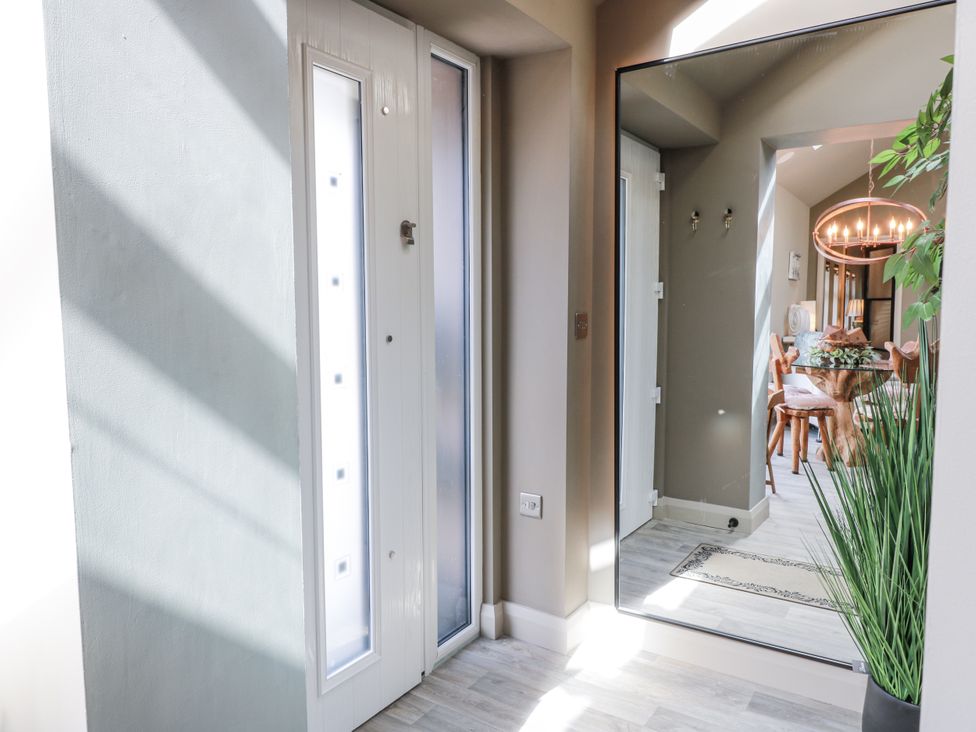 A hallway with a door and mirror leading to a dining area at Scotia At The Brig Annan