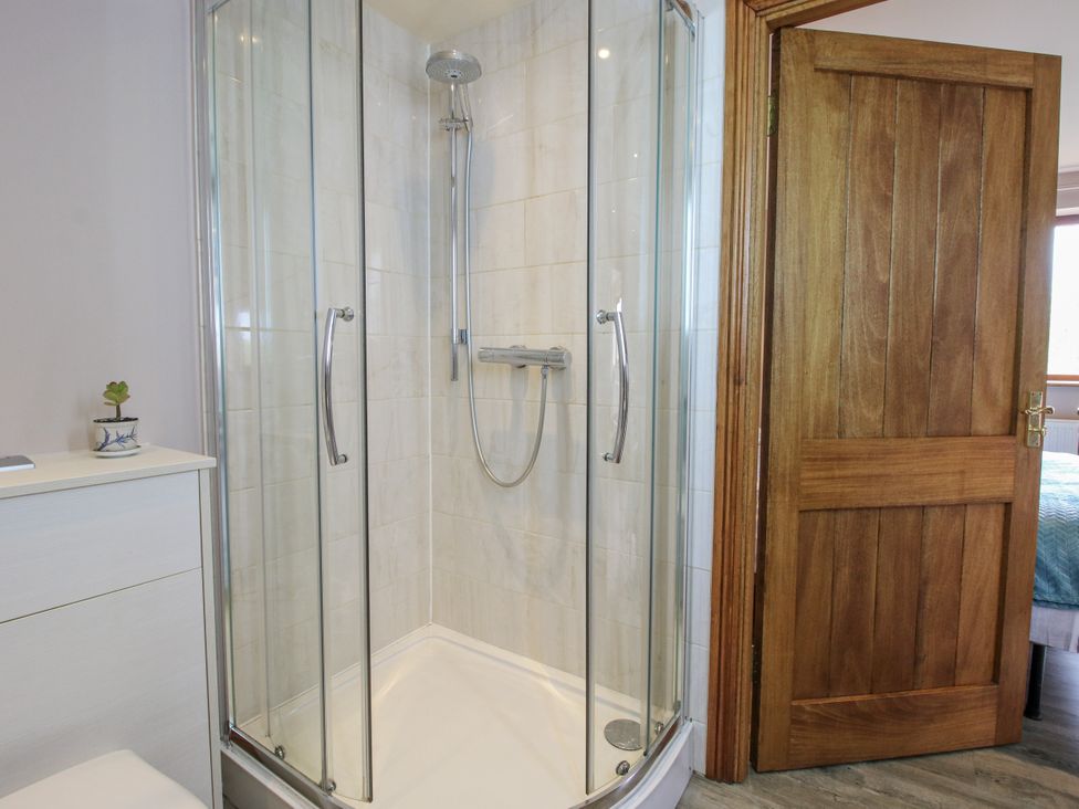 A shower with glass doors and a wooden door at Bluebell Cottage