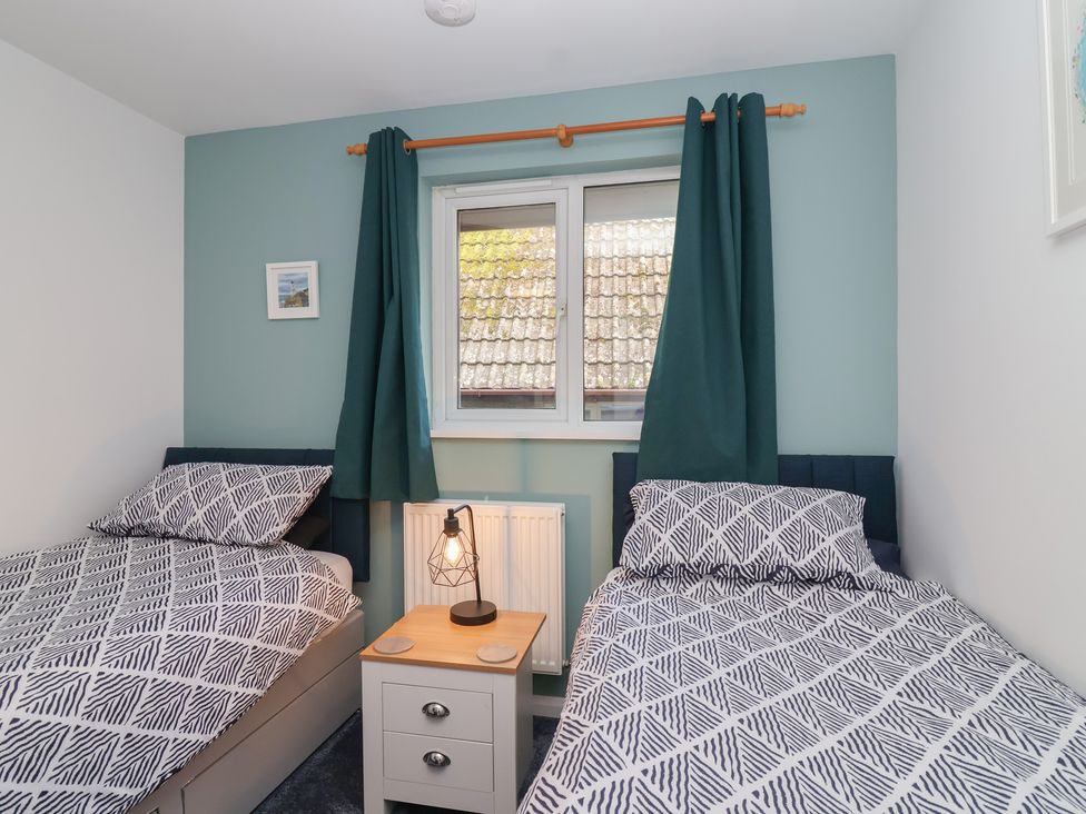A bedroom with two beds, a lamp, and a window at Mayfly Lodge St Tudy
