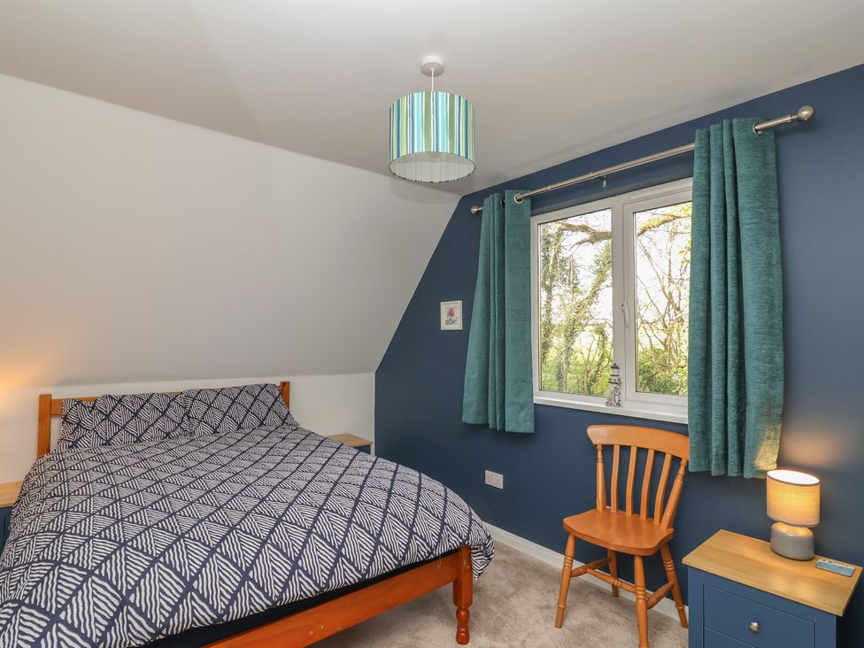 A bedroom with a bed and a chair at Mayfly Lodge in St Tudy