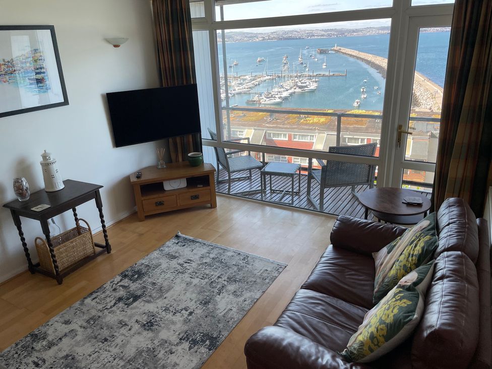 A living room with a television and furniture overlooking the harbor at Snowy Owl View at The Breakwater in Brixham