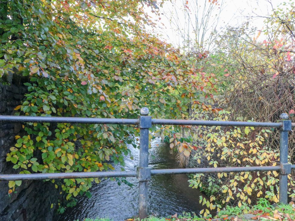 A metal railing overlooking a stream with trees and leaves at Cabin in 