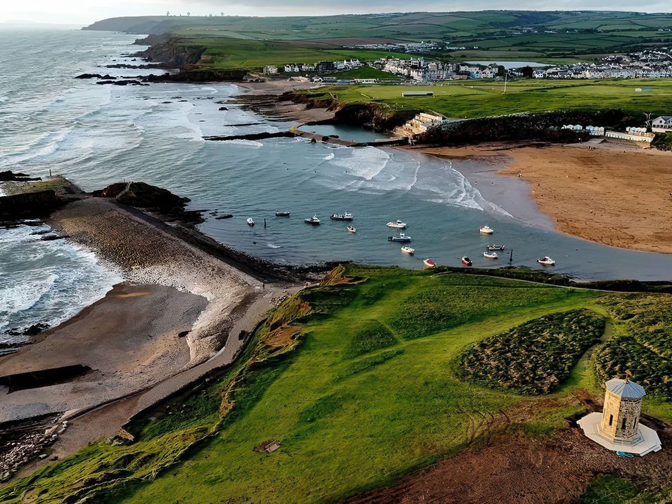 An aerial view of boats in the ocean near a beach and cliff at The Dairy in Bridgerule