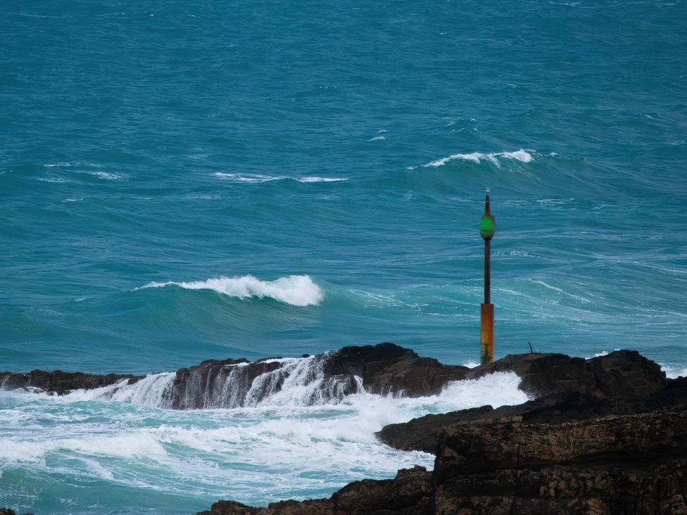 An ocean view with waves and a buoy on a rocky shore at The Dairy in Bridgerule