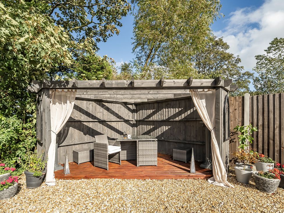 A garden seating area with a table and chairs under a pergola at The Stables in Poulton-le-Fylde