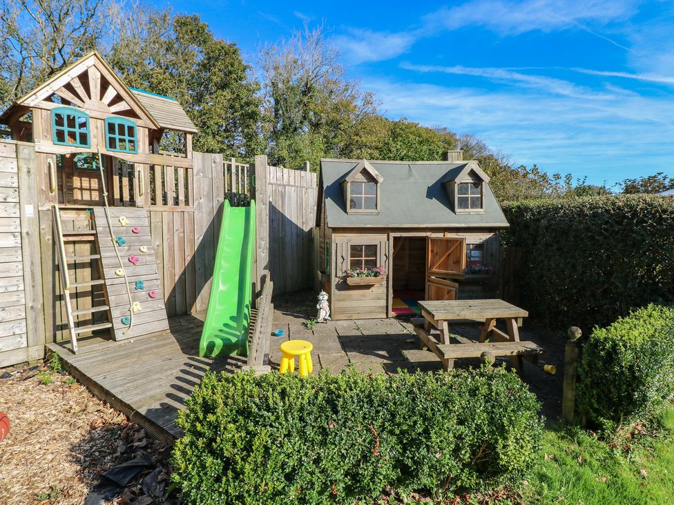 A play area with a wooden playhouse and slide at Carthouse Cottage in Clarbeston Road