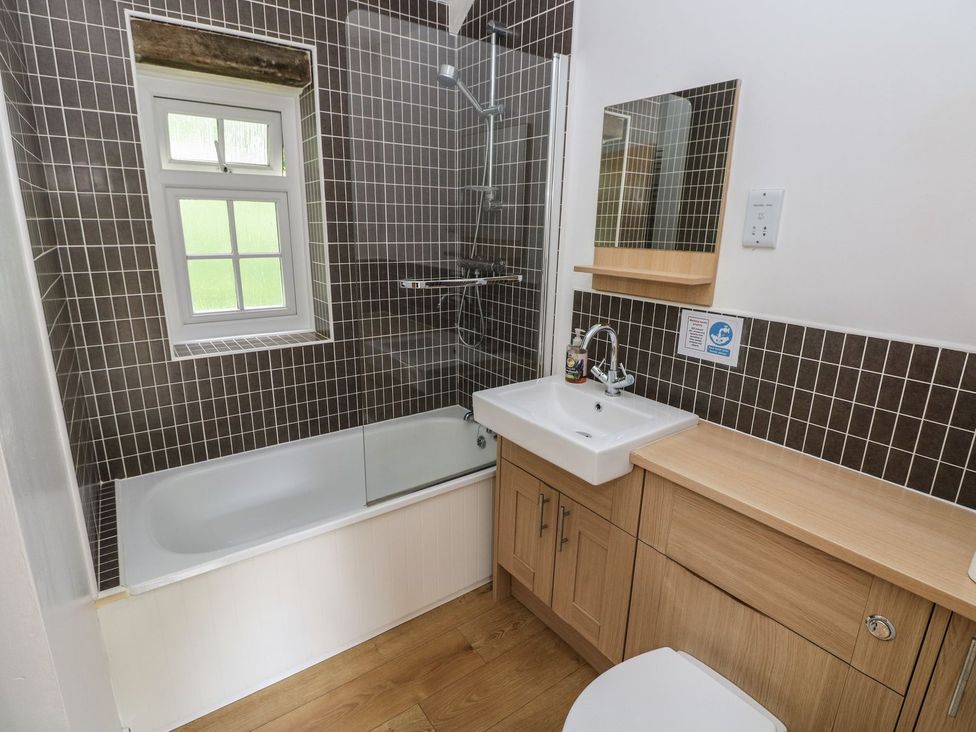 A bathroom with a bathtub, shower, sink, and mirror at Corner Cottage in Clarbeston Road