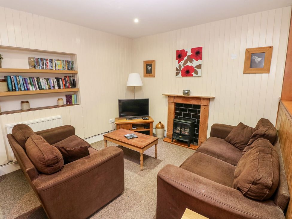 A living room with a television, sofa, and bookshelf at Lake Cottage in Clarbeston Road