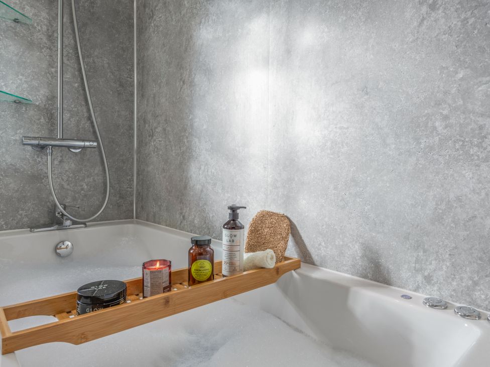 A bathtub with a bamboo tray and various personal care items at Newlands in Yelverton