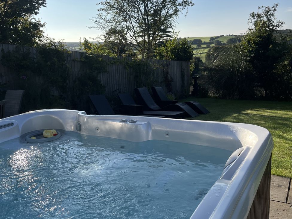 A hot tub and deck chairs in a garden at Newlands in Yelverton