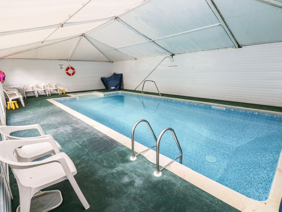 An indoor pool area with a pool ladder and plastic chairs at Rafters Cottage in Clarbeston Road