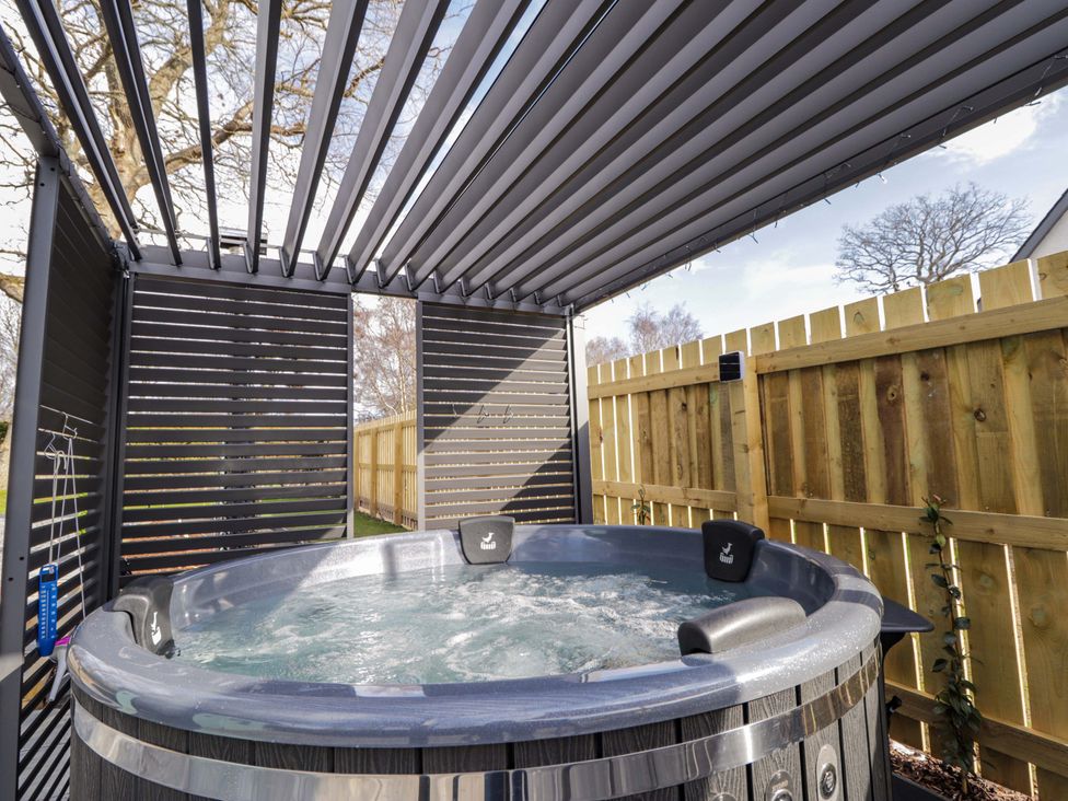 A hot tub with a wooden fence and shelter at Little Oaks in Poyntzfield near Cromarty