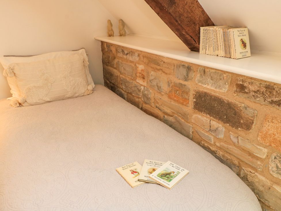A bedroom with a bed and books on the stone wall at The Farmhouse in Langport