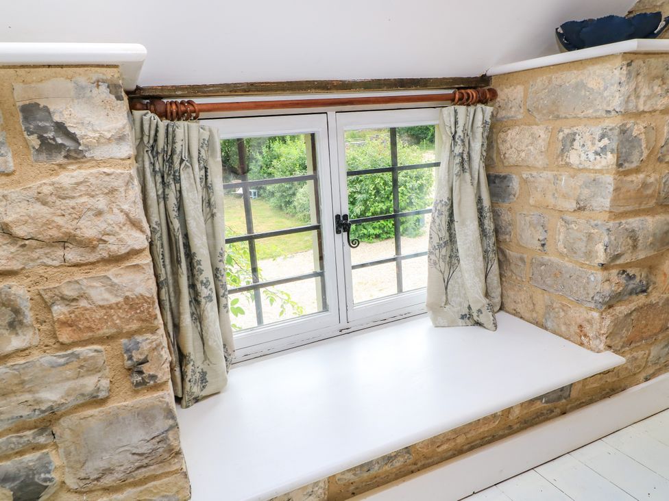 A window with curtains and a stone wall at The Farmhouse in Langport
