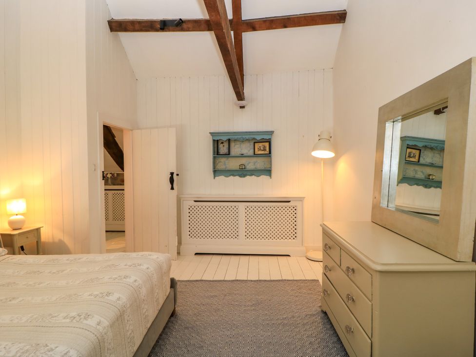 A bedroom with a bed, lamp, dresser, and decorative shelf at The Farmhouse in Langport