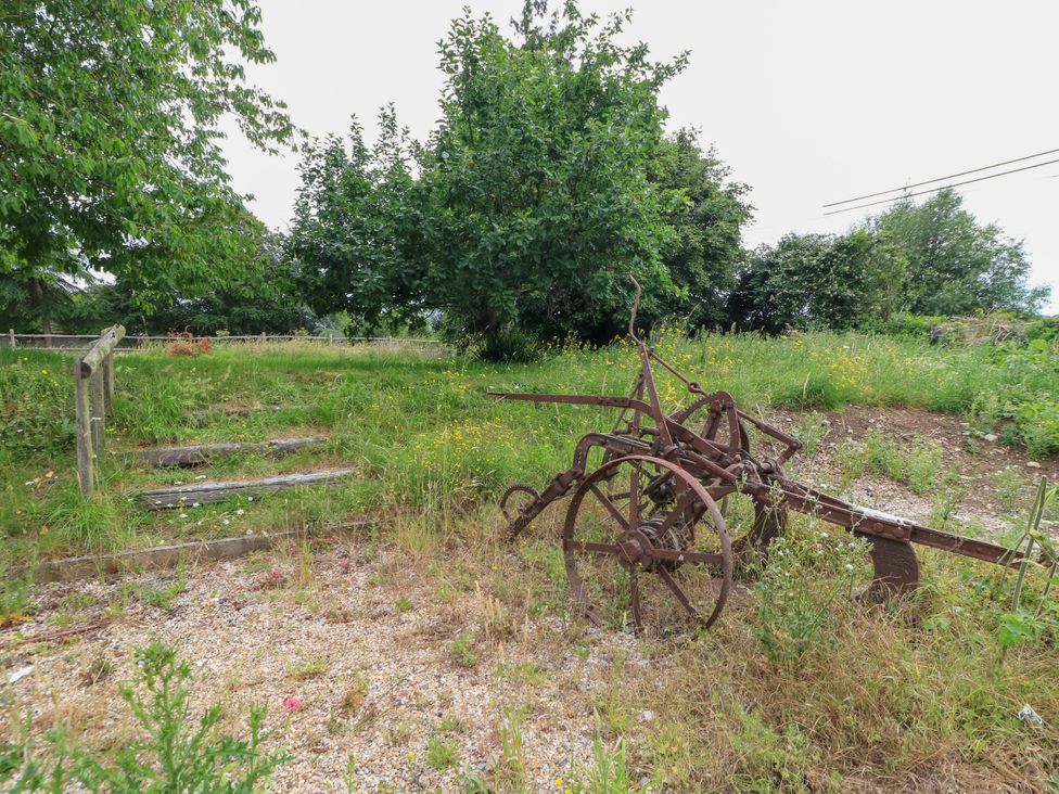 A rusty plow in a grassy area with trees and wooden steps at The Farmhouse in Langport