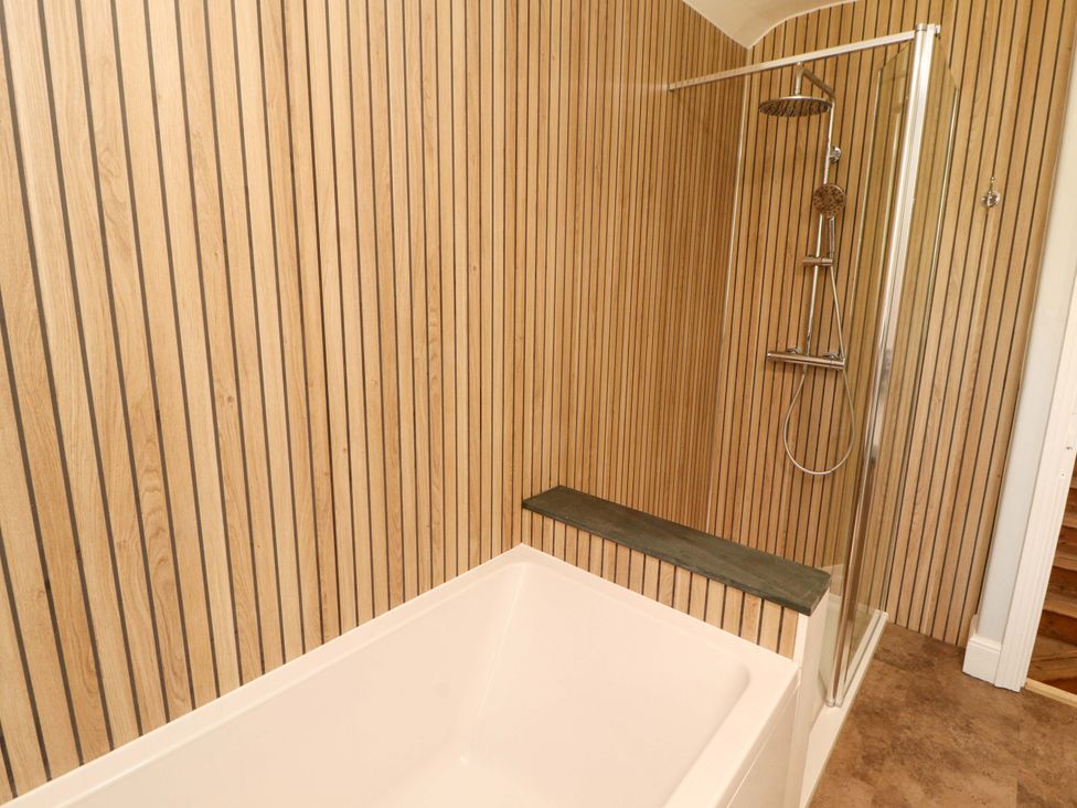 A bathtub and shower area with wooden paneling at East View in Kirkby Stephen