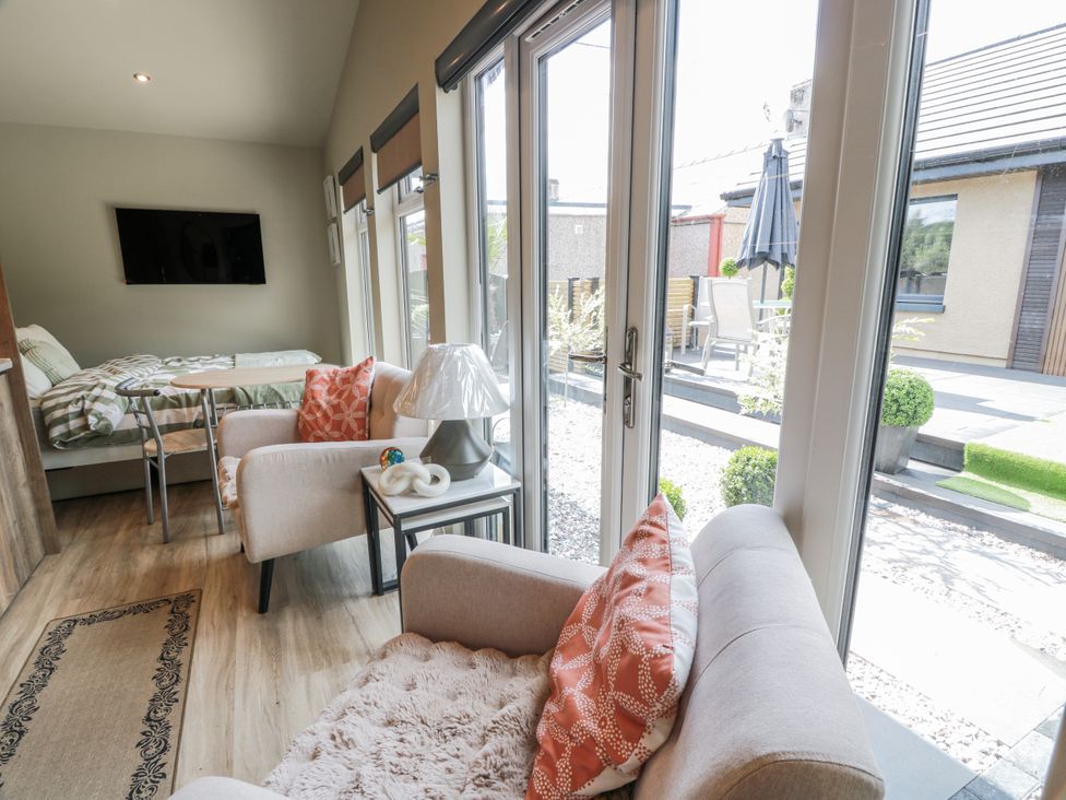A conservatory with a sofa, armchair, table, and television at Cabin At The Brig in Annan