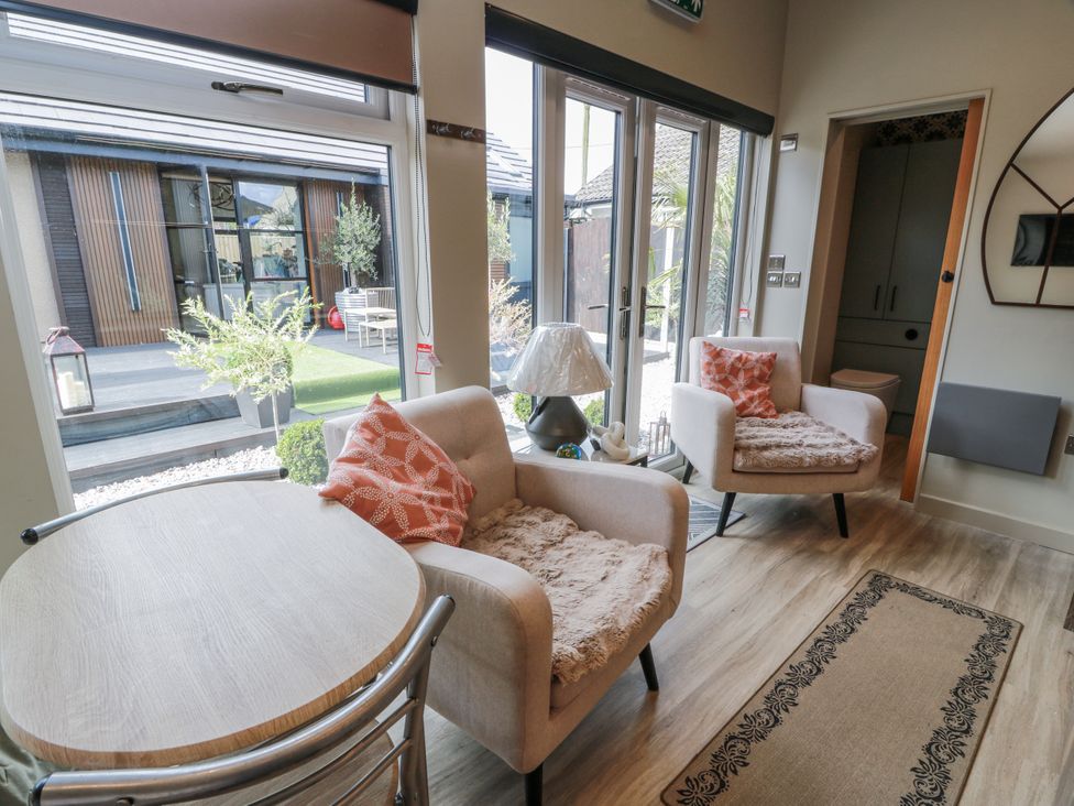 A living room with a table and chairs next to large windows at Cabin At The Brig Annan