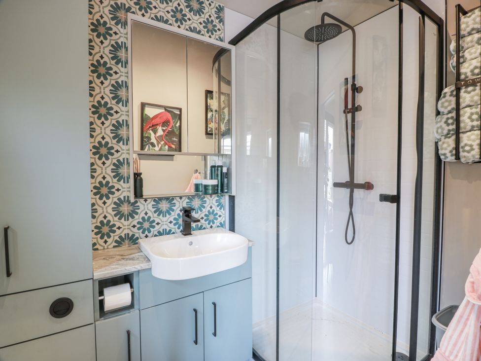A bathroom with a shower, sink, mirror, and cabinet at Cabin At The Brig in Annan
