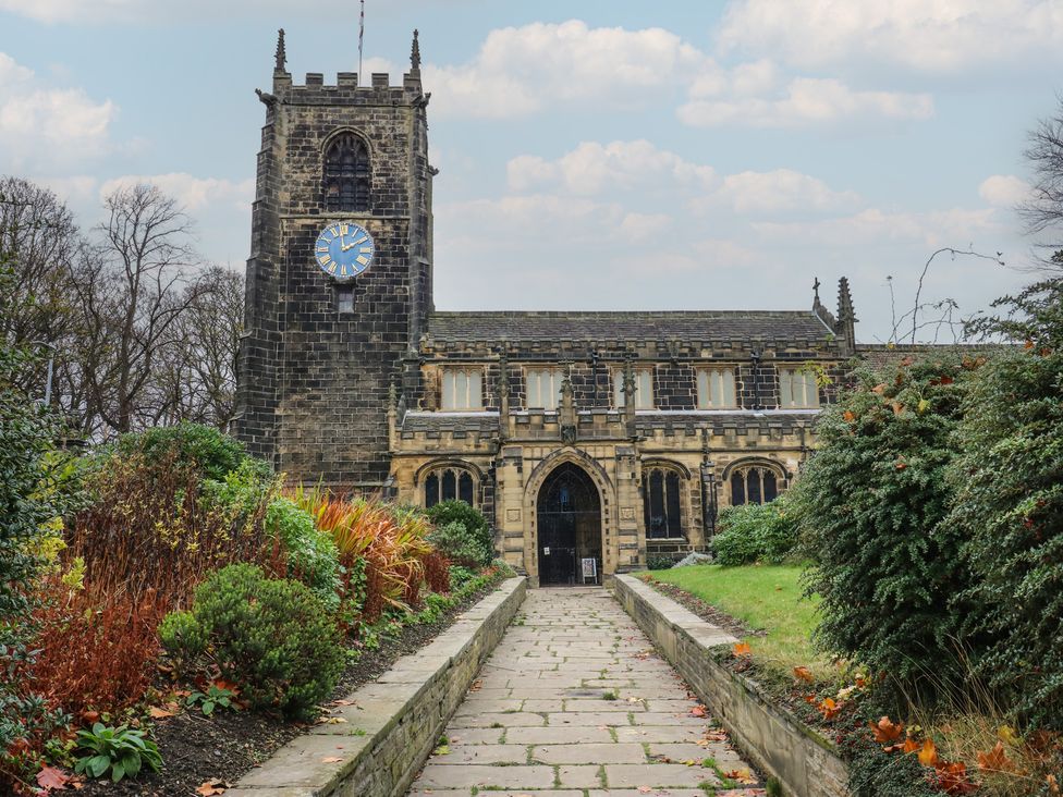 A stone building with a clock tower and gardens in front at Fairfield House Almondbury