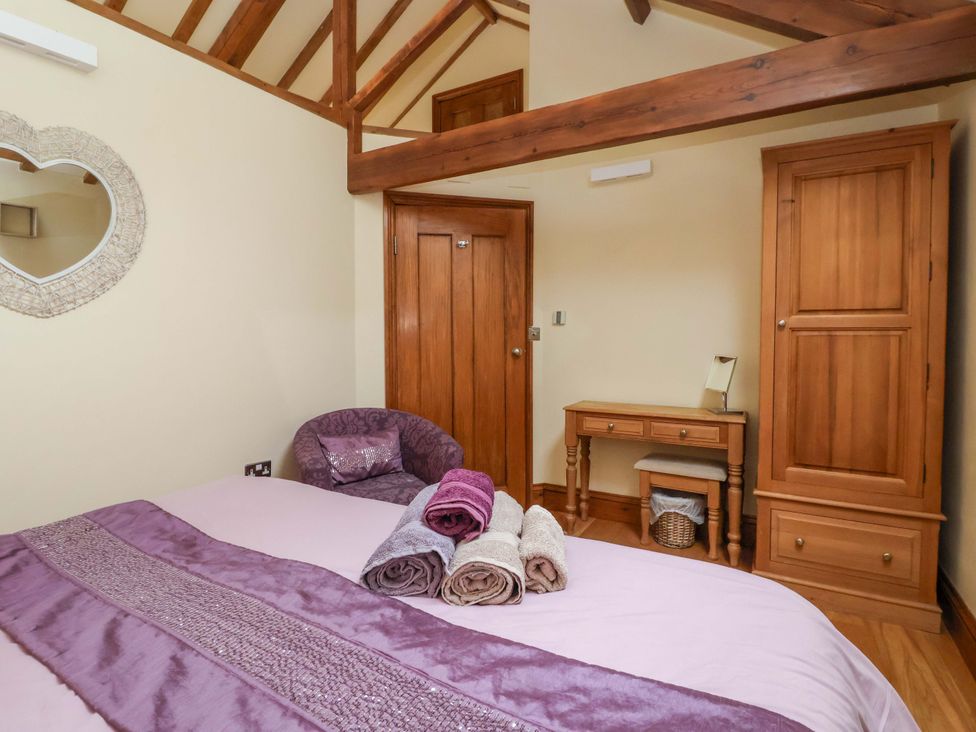 A bedroom with a bed, mirror, chair, table and wardrobe at The Owl Barn Cottage 