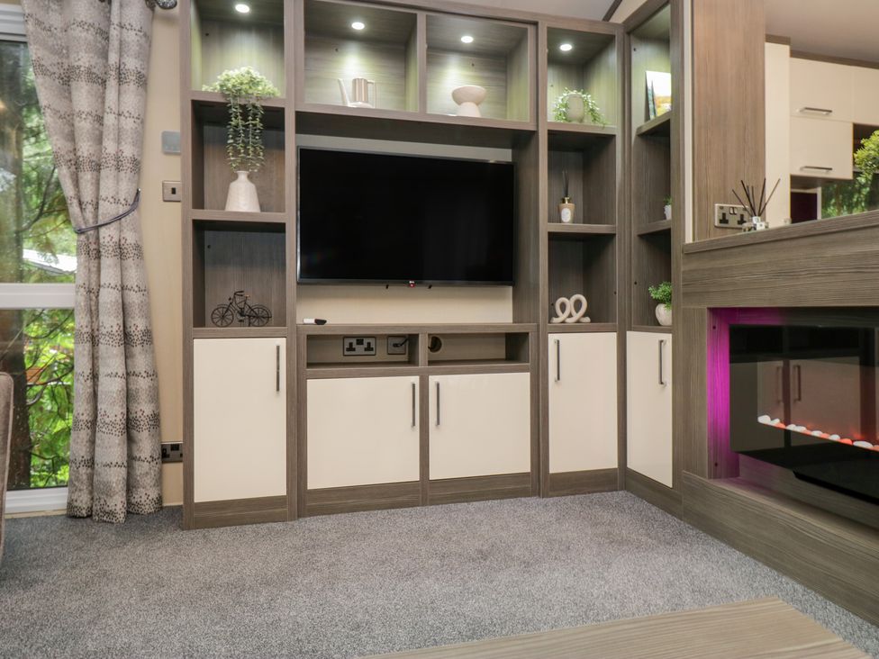 A living room with a television and shelves at Feather Hill Lodge in Windermere
