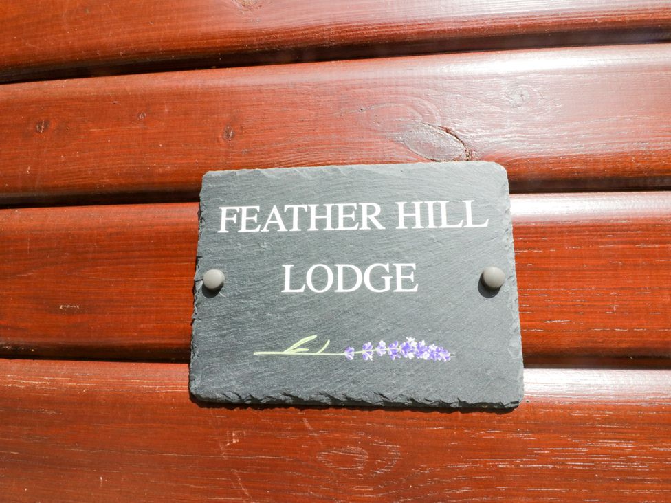 A sign displaying Feather Hill Lodge attached to wood at Feather Hill Lodge White Cross Bay near Troutbeck Bridge