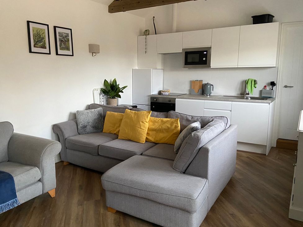 A living room with a sofa and kitchen area at The Cart Shed in Bedford