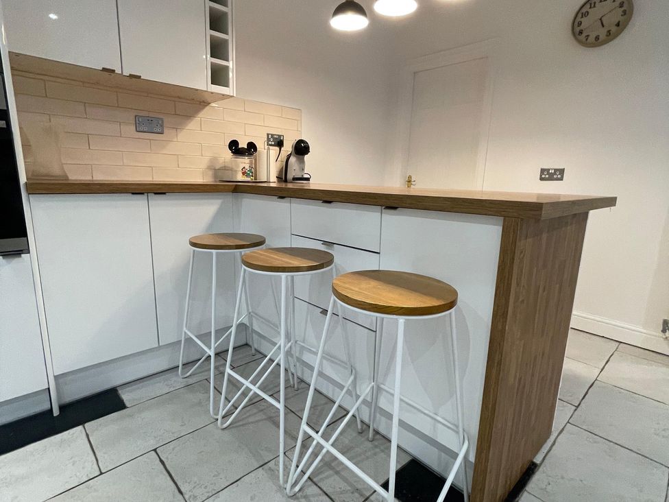 A kitchen with a wooden island and white bar stools at 15A Currier Lane Ashton-under-Lyne