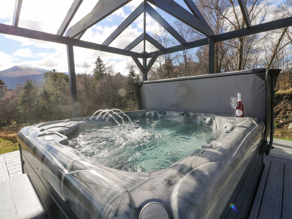A hot tub on a deck with a bottle and glasses at Macgregor Ranch Achnabobane near Spean Bridge