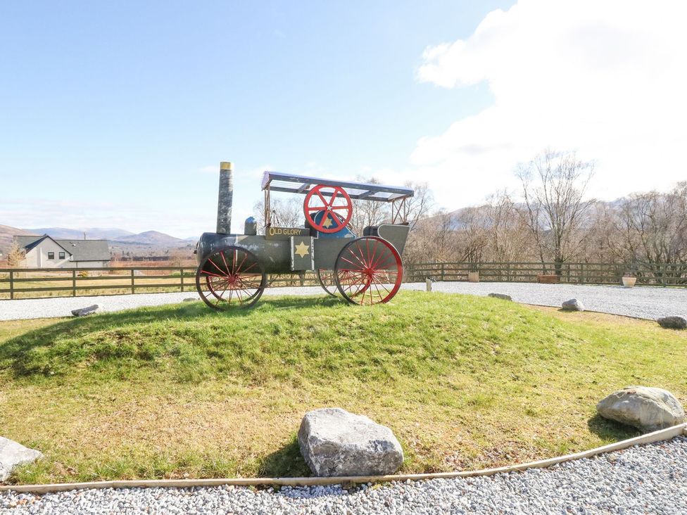 A steam engine on grass with gravel and a fence at Macgregor Ranch Achnabobane near Spean Bridge
