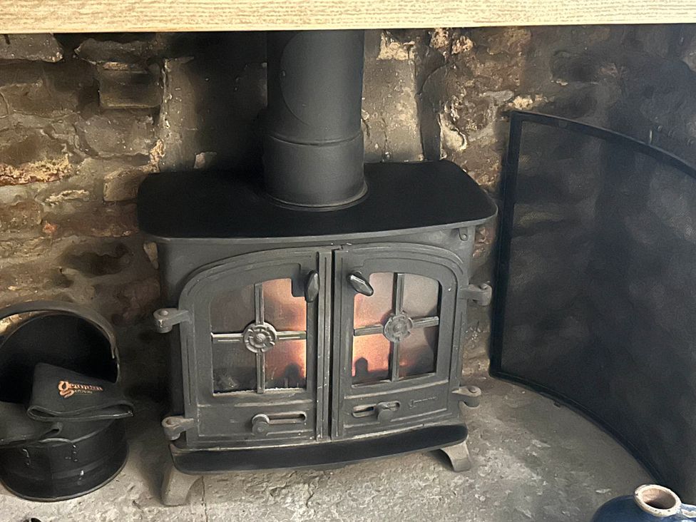 A stove with a fire and a bucket beside it at Redwood Cottage in Blagdon