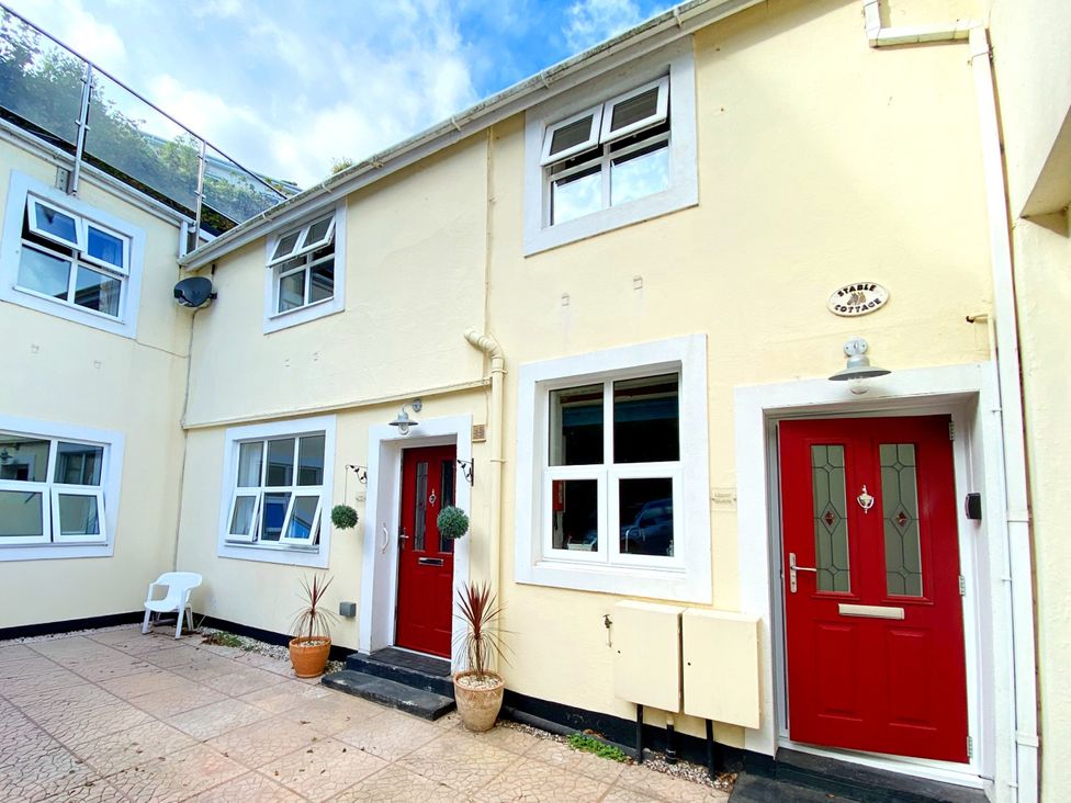 An outdoor view of Stable Cottage with red doors and planters at Lower Stable - The Stables Apartments at Meadfoot Bay in Torquay