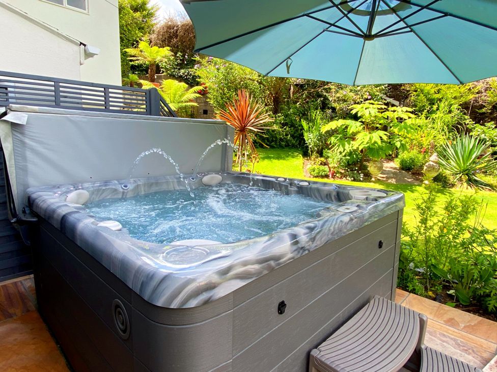 A hot tub with an umbrella and plants in the garden at Muntham Luxury Town House with Hot Tub in Torquay