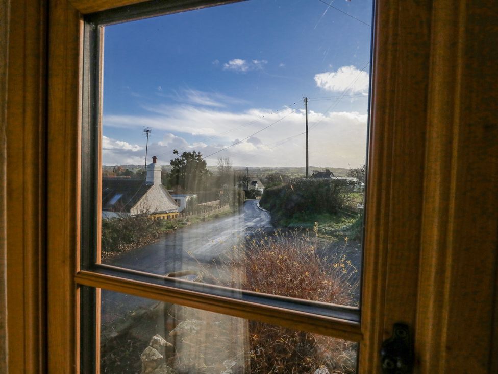 A view of houses and a road through a window at Honeysuckle Cottage in Smallridge Nr. Axminster