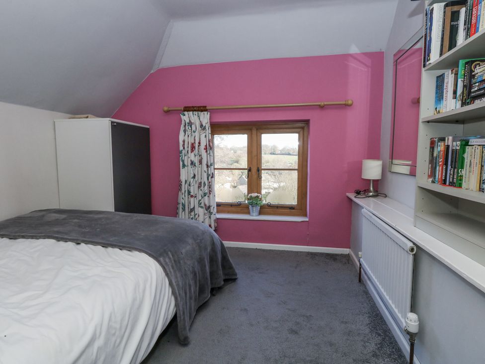 A bedroom with a bed and shelf filled with books at Honeysuckle Cottage in Smallridge Nr. Axminster