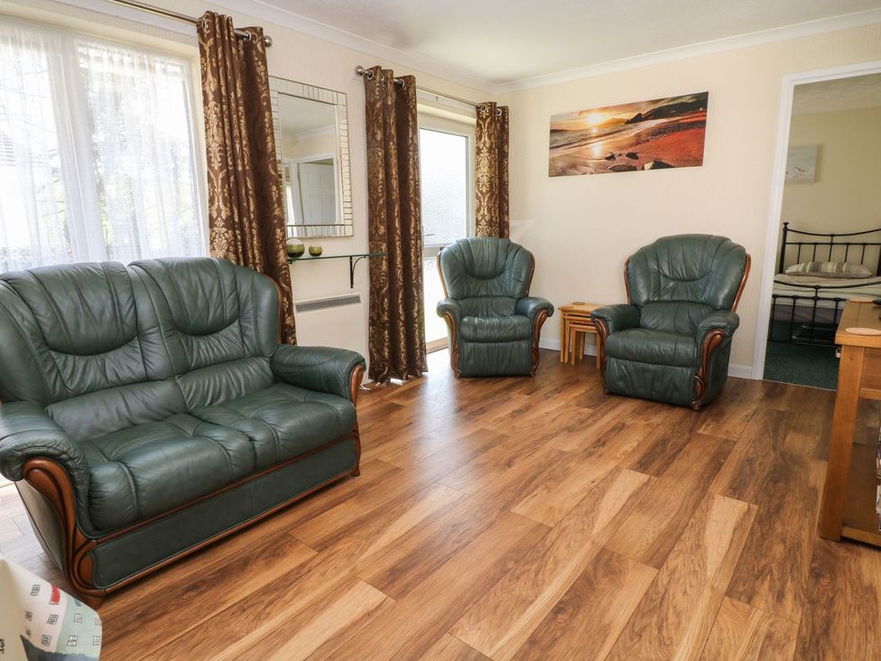 A living room with green leather seating at Willow Lodge in Liskeard