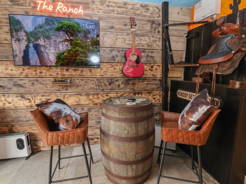 A snug with a television, barrel table, and bar stools at The Ranch in Prestatyn