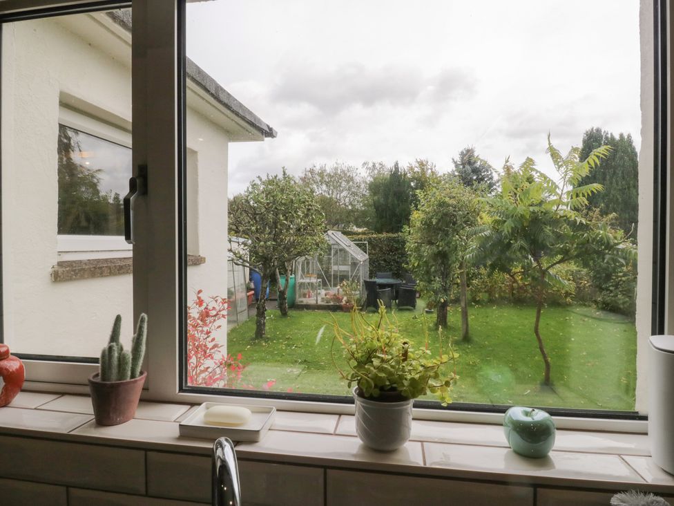 A view of a garden with a greenhouse from a kitchen window at Apple Byrd in Kendal