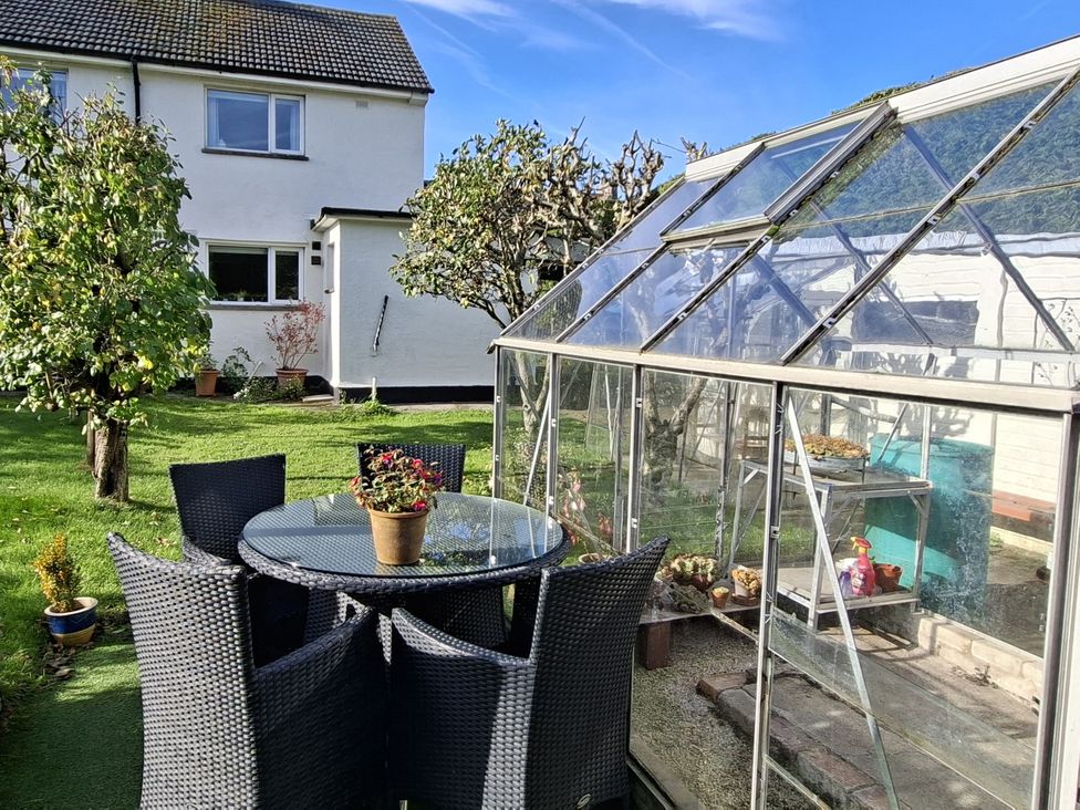 A table and chairs with a greenhouse in the garden at Apple Byrd in Kendal