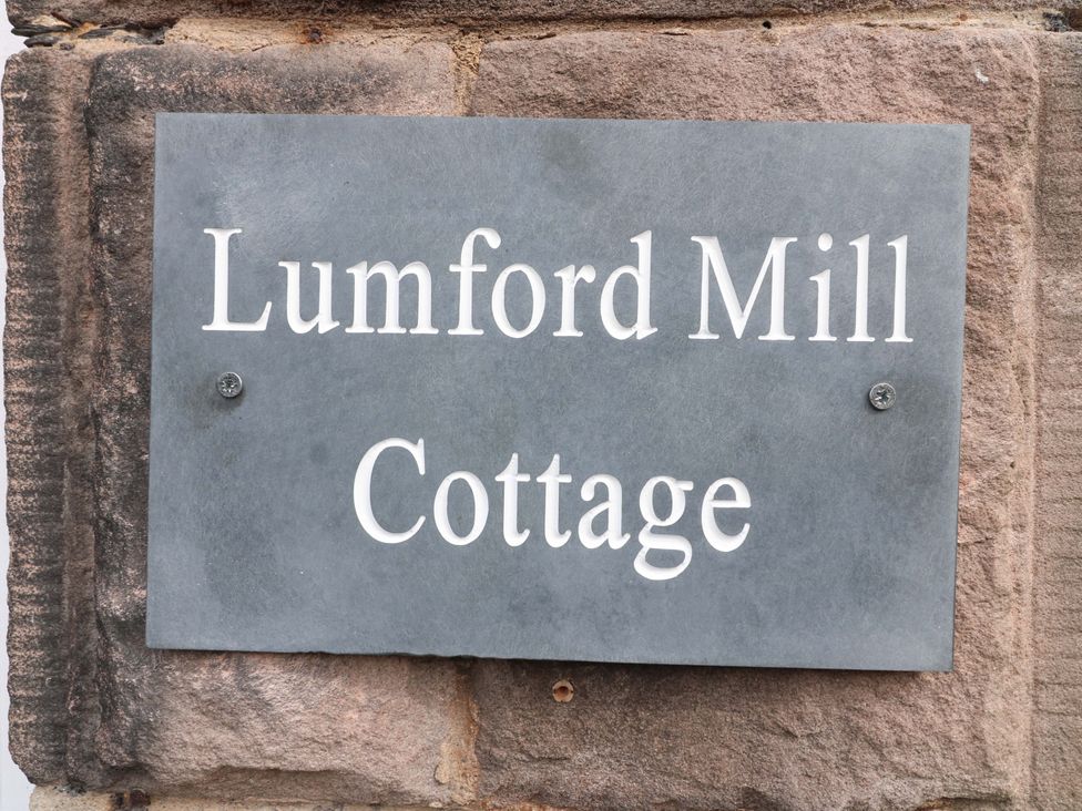 A plaque displaying 'Lumford Mill Cottage' on a stone wall